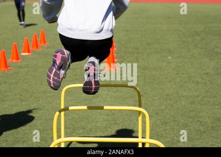 Als Leichtathlet springt über einen gelben Hürde beim Agility Drills auf grünem Rasen Stockfoto