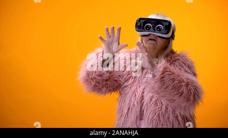 Ältere Frau in lustig Fell und VR-Headset spielen video game, Hi-end Innovationen Stockfoto