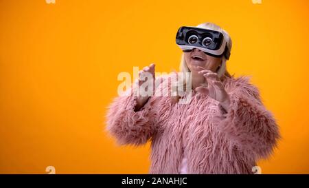 Positive ältere Frau in lustig Fell und VR-Headset spielen video game Technology Stockfoto
