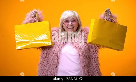 Happy Aging Dame in lustige rosa Fell zeigt Gelb Einkaufstaschen, Geld Stockfoto