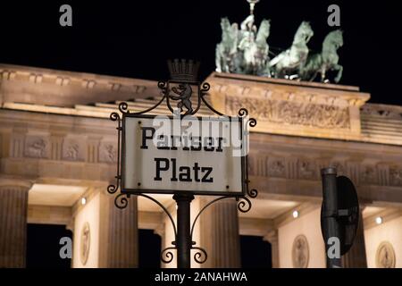 Ein Wegweiser im alten Stil mit dem deutschen Namen Pariser Platz (Pariser Platz), der vor dem beleuchteten Brandenburger Tor in Berlin platziert ist. Stockfoto