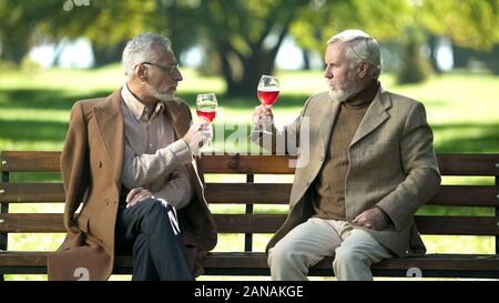 Zwei elegante älteren Herren klirren Gläser Wein im Park, alte Freundschaft Stockfoto