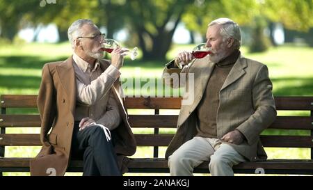 Ältere Männer trinken Rotwein sitzt auf der Bank im Park, alte Freunde tradition Stockfoto