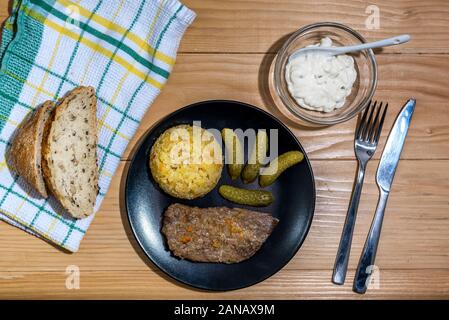 Vorbereitete Rindfleisch Steak mit Reis Risotto, Essiggurken und Soße auf schwarze Platte auf hölzernen Tisch Hintergrund Stockfoto