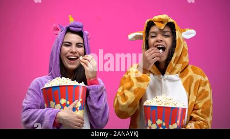 Zwei Frauen in Einhorn und Giraffe pajamas Essen Popcorn und beobachten Komödie Stockfoto