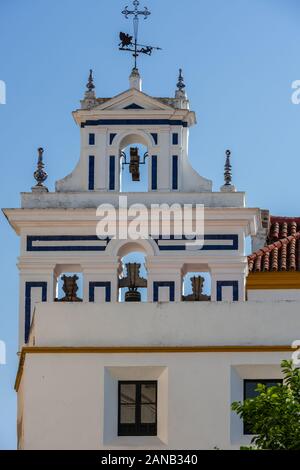 Eine schmiedeeiserne Kreuz und verzierten Wetterfahne top Die weiß getünchten Glockenturm der Iglesia Santiago in der Plaza de Jesus de la Redencion in Sevilla Stockfoto