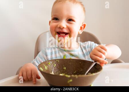 Kleiner Junge allein isst Püree aus einer Platte. Stockfoto