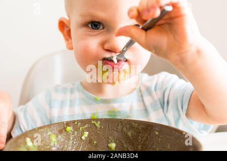 Kleiner Junge allein isst Püree aus einer Platte. Stockfoto