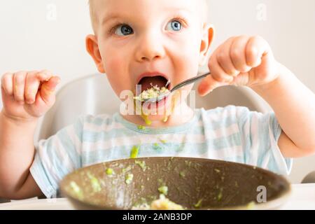 Kleiner Junge allein isst Püree aus einer Platte. Stockfoto