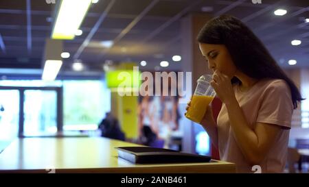 Brünette Frau trinkt Orangensaft aus Kunststoff, Glas, antioxidative Ernährung Stockfoto
