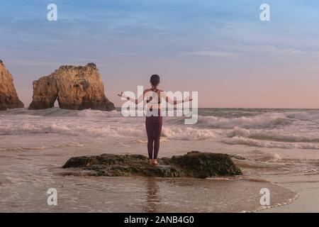 Frau Yoga steht auf einem Felsen am Meer mit Wellen, stehende Yoga dar. Stockfoto