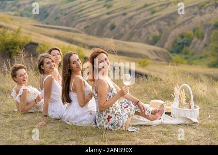 Die Firma fröhliche weibliche Freunde in weißen Kleidern mit Blick auf die grünen Hügel, entspannen Sie bei einem Picknick Stockfoto