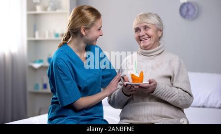 Freiwillige feiert Geburtstag mit älteren Dame holding Kuchen, Patientenversorgung Stockfoto