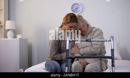 Junge weibliche Umarmen deaktiviert Großmutter sitzt auf dem Bett, Gehhilfe rehab Stockfoto