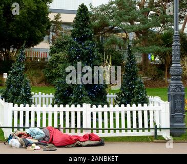 Ein Obdachloser schläft neben einem Weihnachtsbaum in Bournemouth's Winter Gardens Stockfoto
