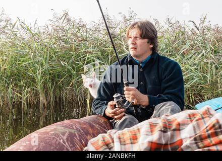 Fischer Fänge Fische vom Boot aus auf schönen kleinen Fluss in den frühen Morgenstunden bei Sonnenaufgang mit seiner Katze. Stockfoto