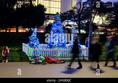 Ein Obdachloser schläft neben einem Weihnachtsbaum in Bournemouth's Winter Gardens Stockfoto