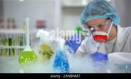 Lab Assistant Beobachtung Reaktion des Rauchens Kolben durch die Lupe Stockfoto