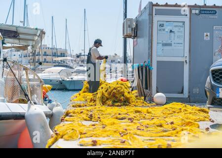 Naxos, Griechenland - 14 August 2019; griechische Kykladen Insel, wo Fischer prüft und repariert helle gelbe Fischernetze am Wharf neben dem Boot. Stockfoto