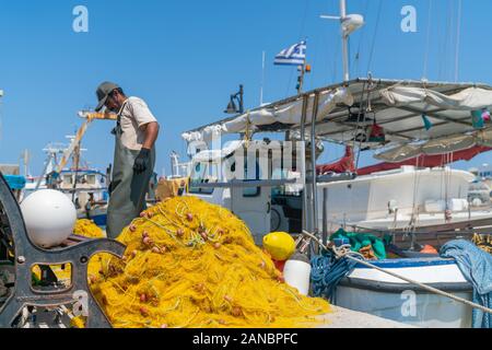 Naxos, Griechenland - 14 August 2019; griechische Kykladen Insel, wo Fischer prüft und repariert helle gelbe Fischernetze am Wharf neben dem Boot. Stockfoto