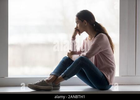 Frustrierte junge Frau auf Fensterbank, zu Hause zu sitzen. Stockfoto