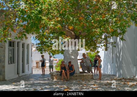 Filoti Naxos - 13. August 2019: Gruppe junger Erwachsener Touristen nehmen Pause im Schatten der Platanen zwischen Gebäude an der Oberseite des Hügels. Stockfoto