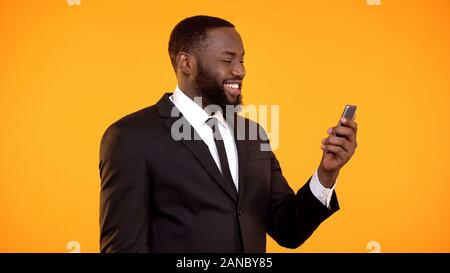 Fröhliche schwarzer Geschäftsmann empfangen Nachricht am Telefon und lächelnd, Anwendung Stockfoto