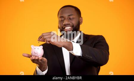 Lächelnd afrikanisch-amerikanischen Geschäftsmann im Anzug, Münze in Sparschwein, Kaution Stockfoto