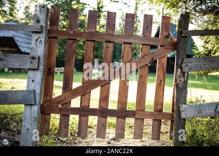 Alte Braune hölzerne Tor und Zaun um einen grünen Garten Stockfoto