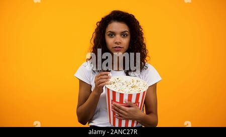 Schöne afroamerikanischen Frau essen Popcorn auf gelbem Hintergrund Stockfoto
