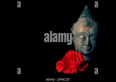 Frieden und Liebe. Traditionelle Meditation Buddha Kopf mit roten Rosen isoliert auf schwarzen Hintergrund Copyspace. Wunderschönes friedliches Bild. Ruhigen buddhistischen Geist Stockfoto