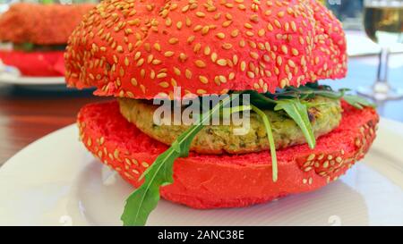 Fast Food auf einem Teller, vegetarischer Kakteenburger mit Raketenblättern, serviert in rotem Weizenbun mit Sesamsamen. Stockfoto