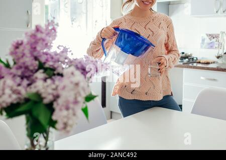 Frau gießen gefiltertes Wasser aus der Kanne in Glas auf Küche. Moderne Küche Design. Gesunder Lebensstil Stockfoto