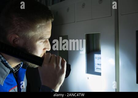 Nahaufnahme von einem Elektriker überprüfen Ein Sicherungskasten mit einer Taschenlampe Stockfoto