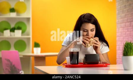 Schöne Dame beißen leckere Cheeseburger, süsse Limonade trinken stehen auf Tabelle Stockfoto