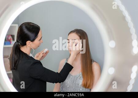 Make-up-Künstler macht Make-up, um die Frau mit blauen Augen Mit Pinsel und Lidschatten Stockfoto