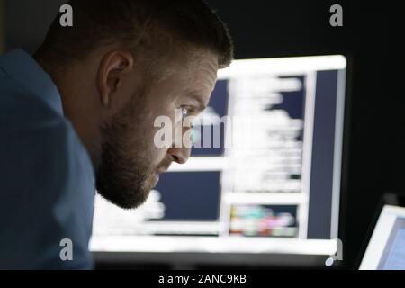 Programmierer arbeiten bis spät in die Nacht auf mehreren Bildschirmen Stockfoto