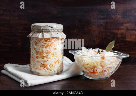 Hausgemachten Sauerkraut mit Karotten im Glas und Schüssel auf einem dunklen Hintergrund. Fermentierter Lebensmittel. Mariniertes Gemüse. Stockfoto