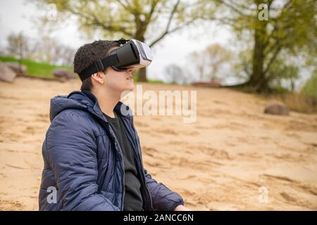 Ein junger Mann mit VR-Brille sitzt auf einem Strand Stockfoto