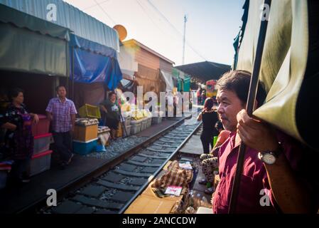 Mae Klong/Thailand-08December2019: Mae Klong Bahnhof mit Gleisen und Zügen, die durch den täglichen Markt führen, mit Anbietern, die alles verkaufen. Stockfoto