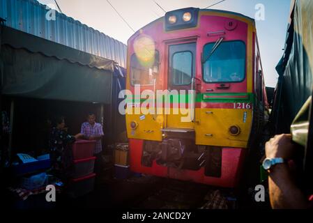 Mae Klong/Thailand-08December2019: Mae Klong Bahnhof mit Gleisen und Zügen, die durch den täglichen Markt führen, mit Anbietern, die alles verkaufen. Stockfoto