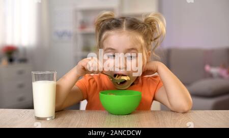 Gerne kleine Mädchen essen Cornflakes mit Milch sitzen home Tabelle, gesundes Essen Stockfoto
