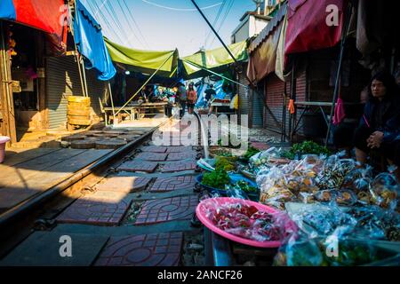 Mae Klong/Thailand-08December2019: Mae Klong Bahnhof mit Gleisen und Zügen, die durch den täglichen Markt führen, mit Anbietern, die alles verkaufen. Stockfoto