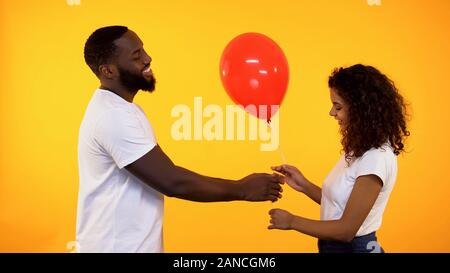 Lächelnd afro-amerikanischer Mann präsentiert Ballon zu cute woman, Geburtstag, Geschenk, Datum Stockfoto