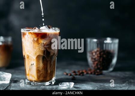 Milch wird ausgegossen in Eiskaffee auf einen dunklen Tisch Stockfoto