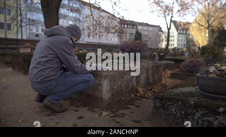 Junge Mann in der Nähe von Grab sitzen auf alten Friedhof betete, Trauer für die Angehörigen Stockfoto