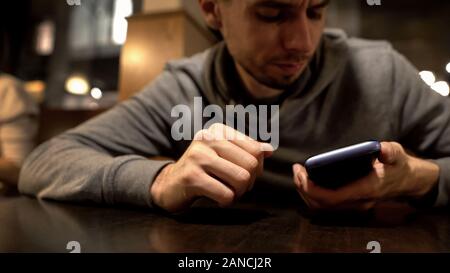 Zornigen Mann mit Blick auf Telefon, Empfangen von Bill von der Bank nach Partei, Kreditkarte Stockfoto