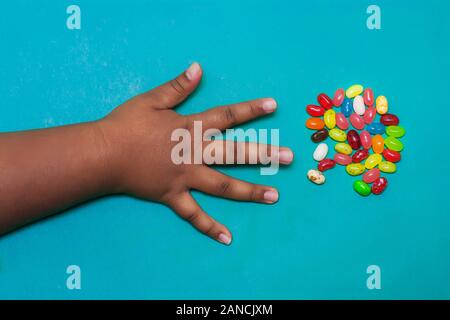 Die Kinder Arm und Hand mit den Fingern verteilen, mit Fruchtgeschmack Süßigkeiten von einem kleinen Dienst zu ergreifen. Stockfoto