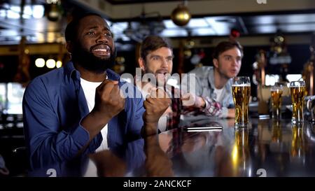 Overemotional afro-amerikanischer Mann Zujubeln für Lieblingsmannschaft mit Freunden in der Bar Stockfoto