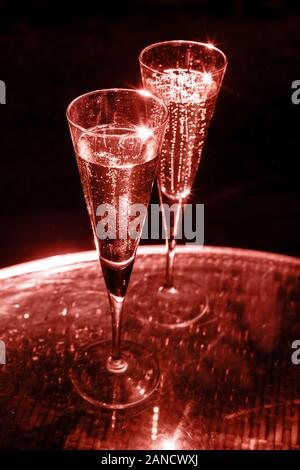 Zwei Gläser Champagner auf den Glastisch auf schwarzem Hintergrund. Lebende Korallen Thema - Farbe für das Jahr 2019 Stockfoto